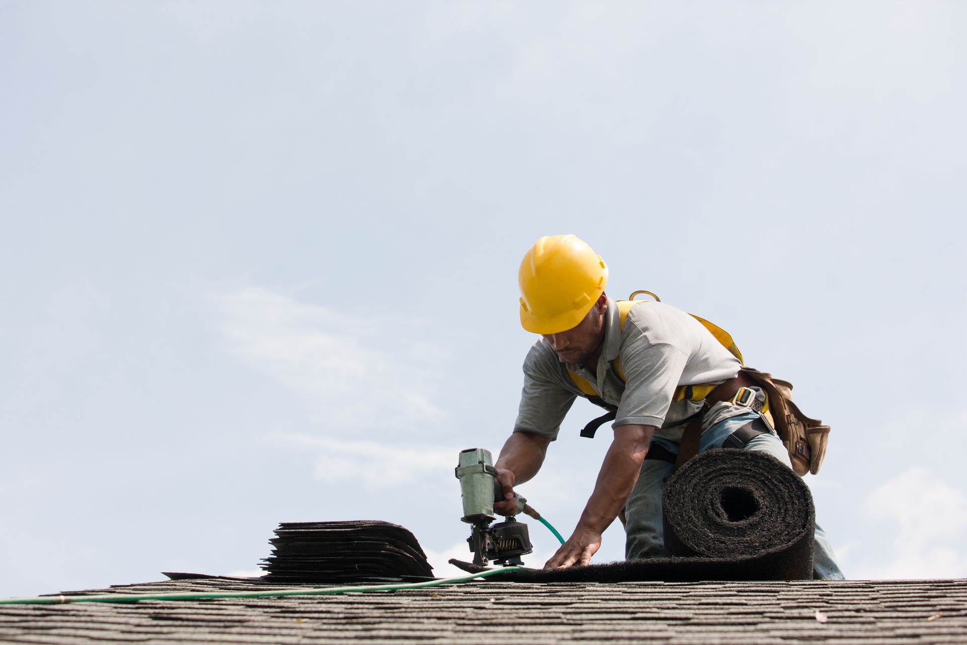 A man wearing a hard hat is working on a roof.