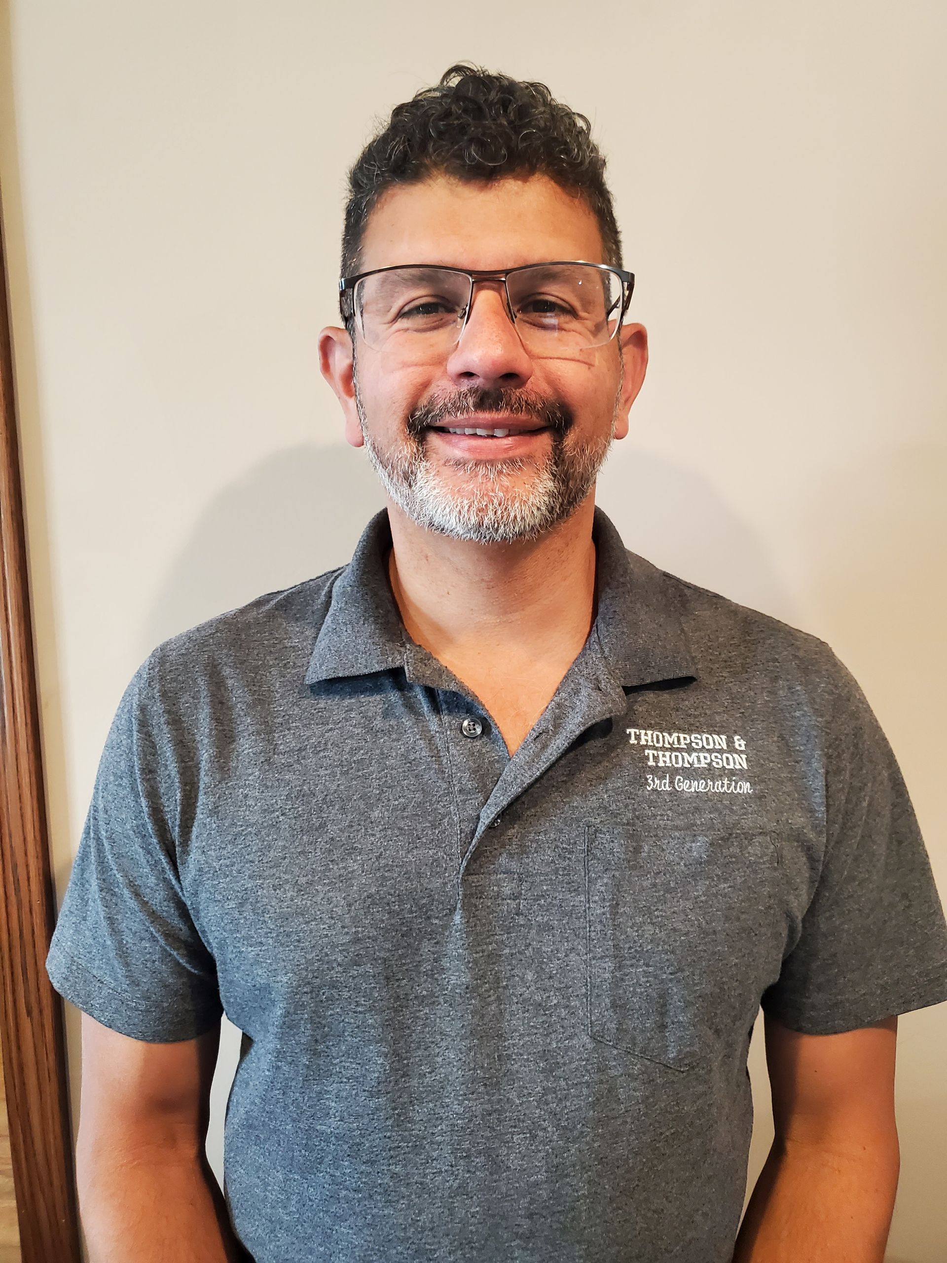 A man with a beard and glasses is wearing a grey shirt and smiling.