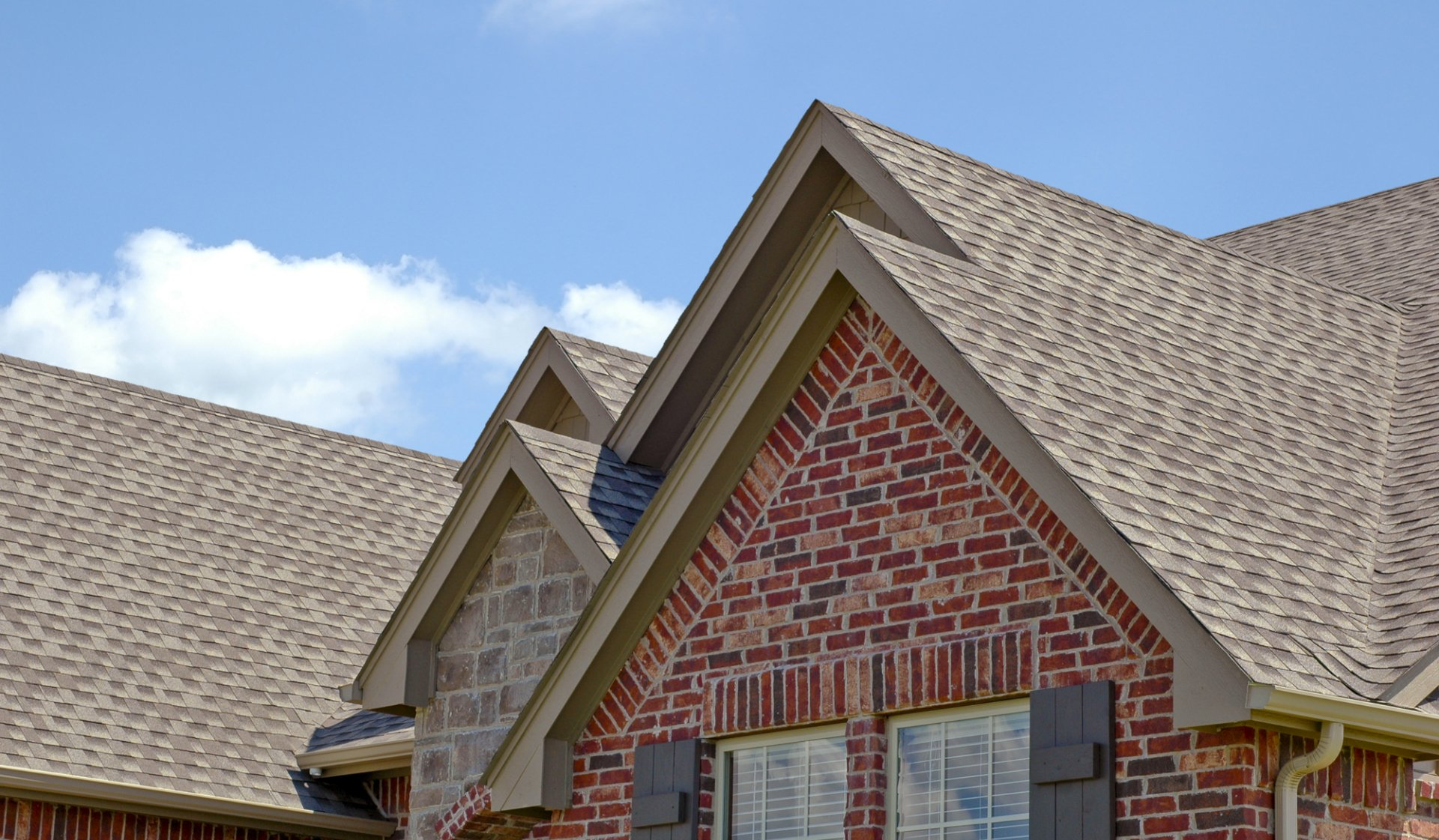 A brick house with a brown roof and a blue sky in the background.