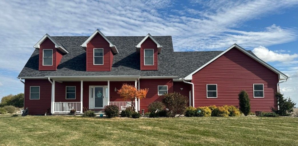 A large red house with a gray roof is sitting on top of a lush green field.