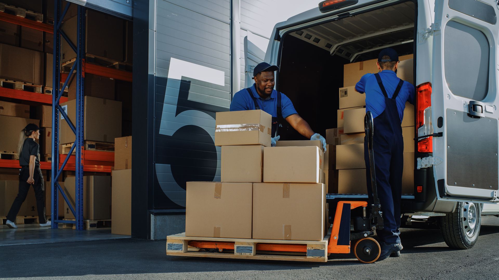 Two men are loading boxes into a van in a warehouse.