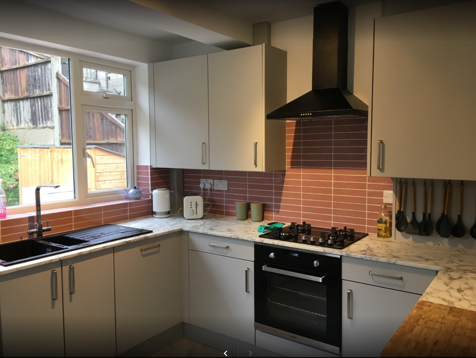 A kitchen with white cabinets , a stove , a sink , and a window.