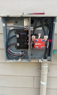 Open electrical panel with wires and breakers mounted on an exterior wall.