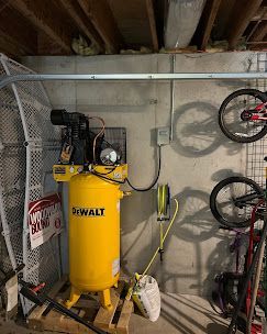 Yellow DeWalt air compressor in a basement, with bicycles on wall and hose.