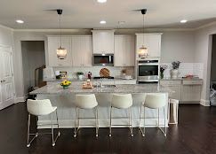 A modern kitchen with a large island, white cabinets, granite countertops, and four barstools.