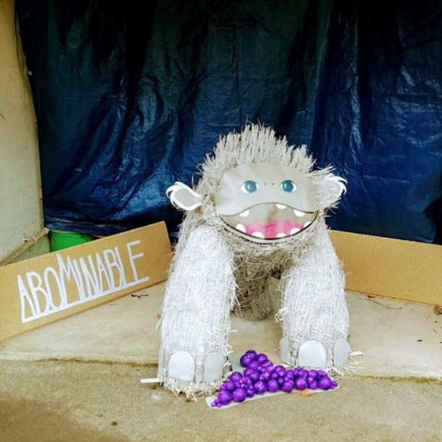 A fuzzy white abominable snowman sculpture with purple grapes in a garage.