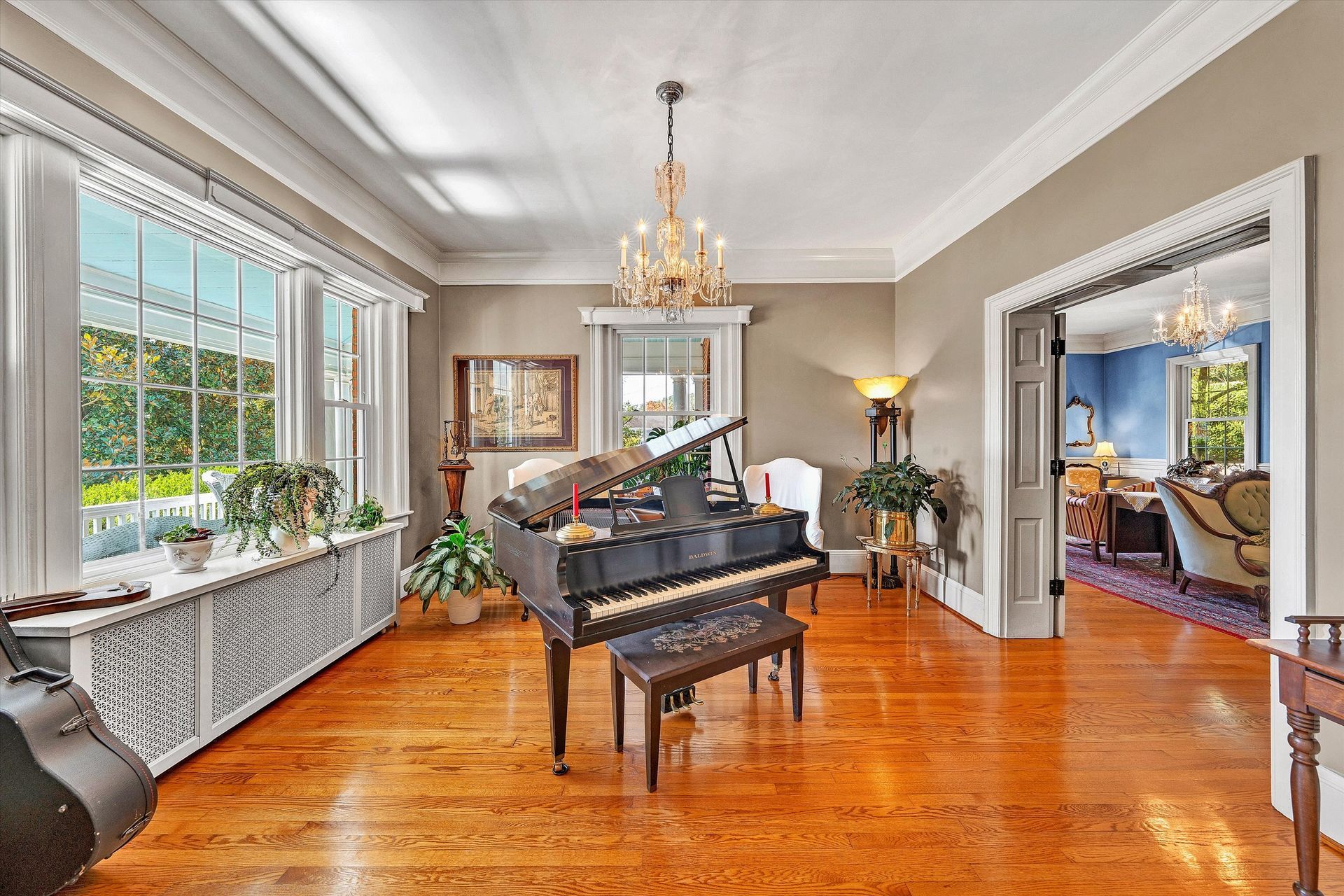 Elegant living room with a black grand piano, chandelier, hardwood floors, and large windows