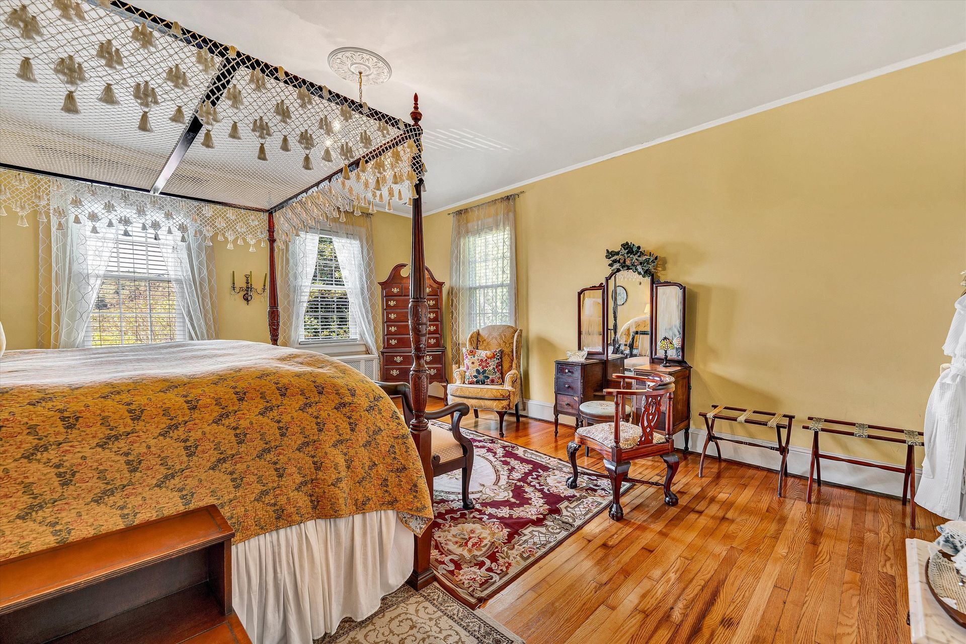 Elegant bedroom with four-poster bed, floral rug, vanity, and warm yellow walls