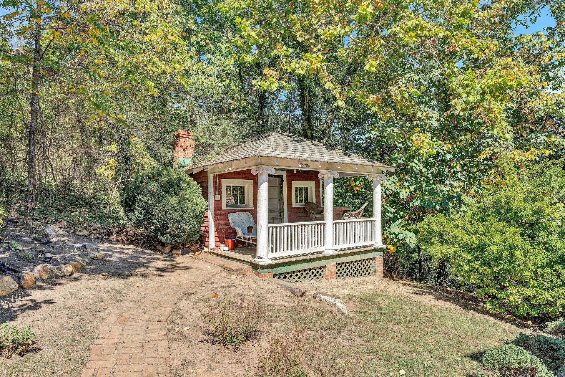 Small white gazebo on a wooded hillside, with a dirt path and autumn trees around it