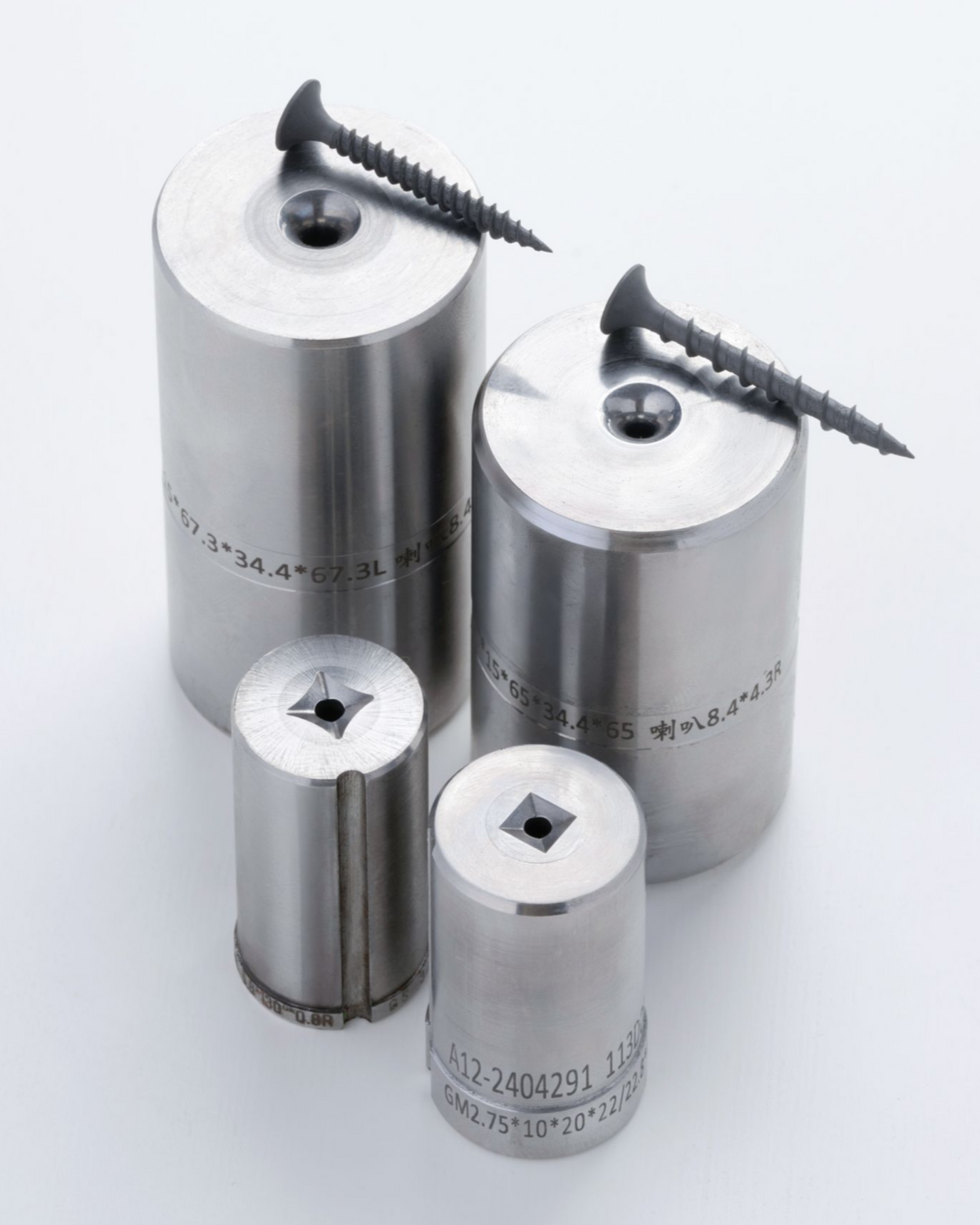 Four shiny metal dies with square holes, screws on top, on a white surface.