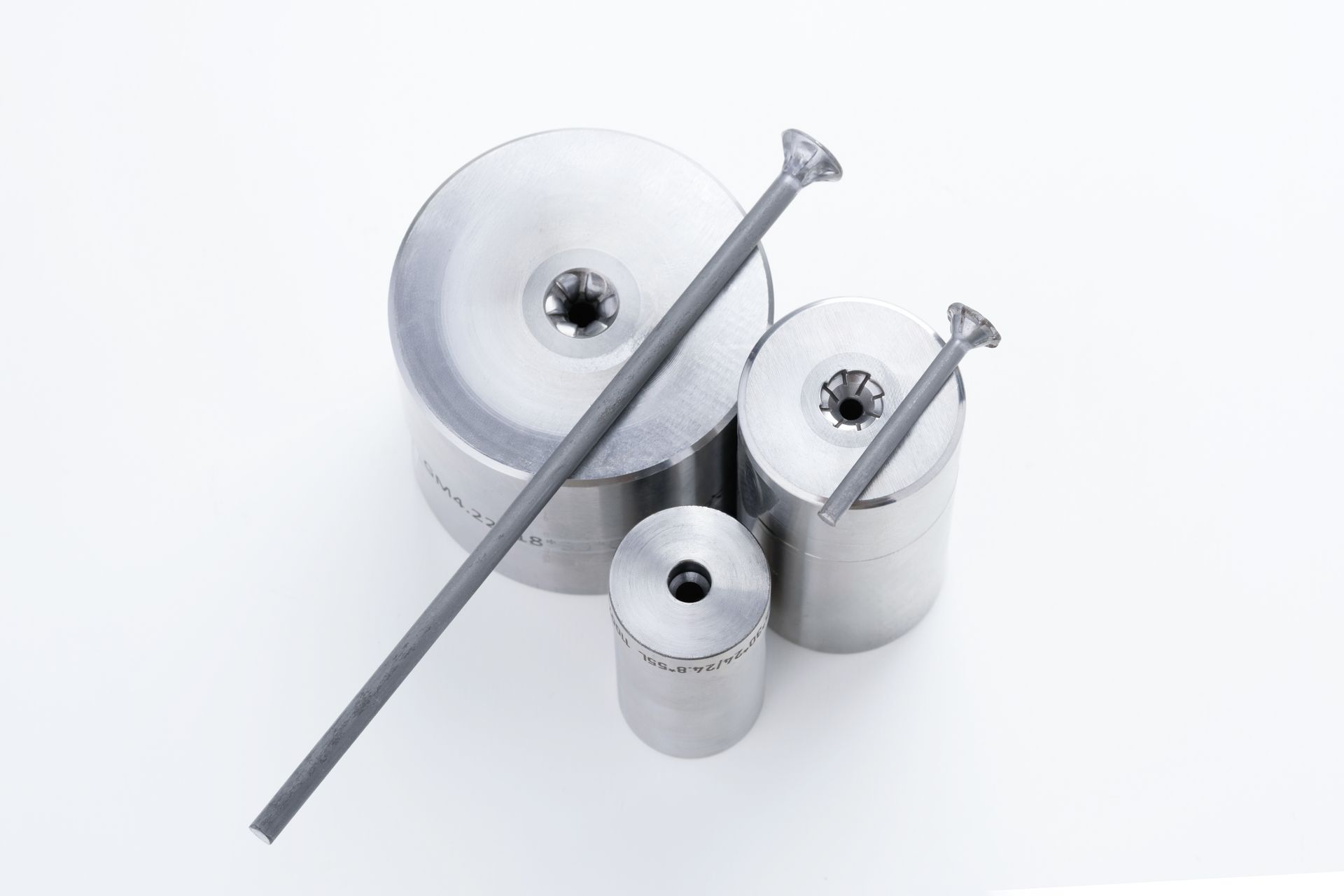 Three metal dies and two gray rods, against a white background.