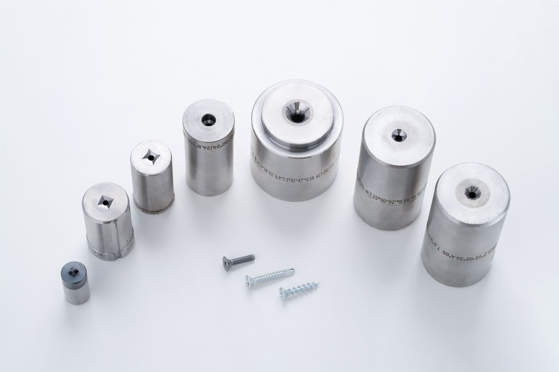 Steel dies of various sizes with screw fasteners on a white surface.