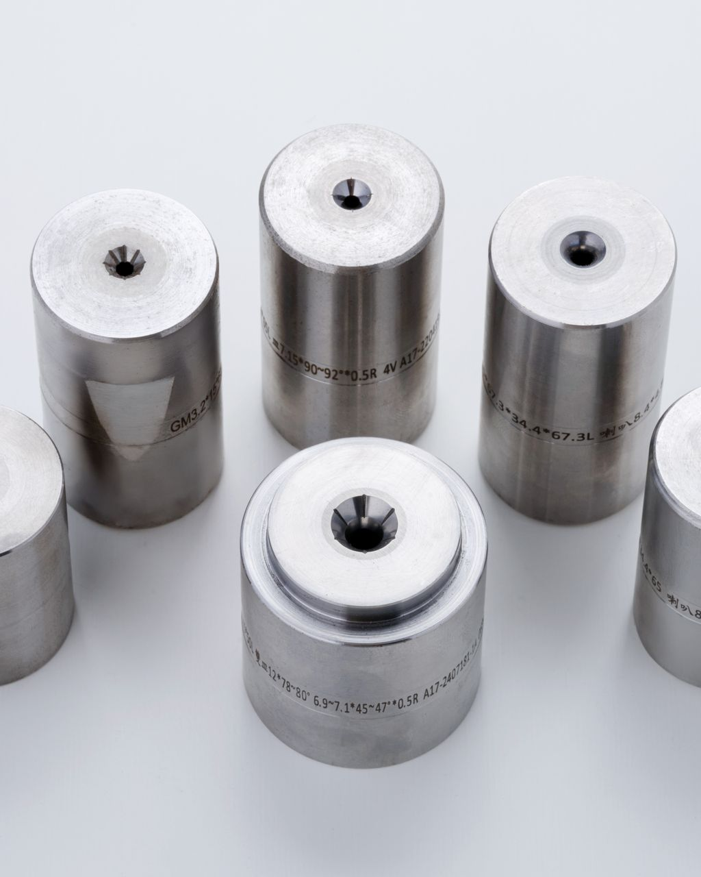 Six cylindrical metal dies with a small hole on top, arranged on a white surface.