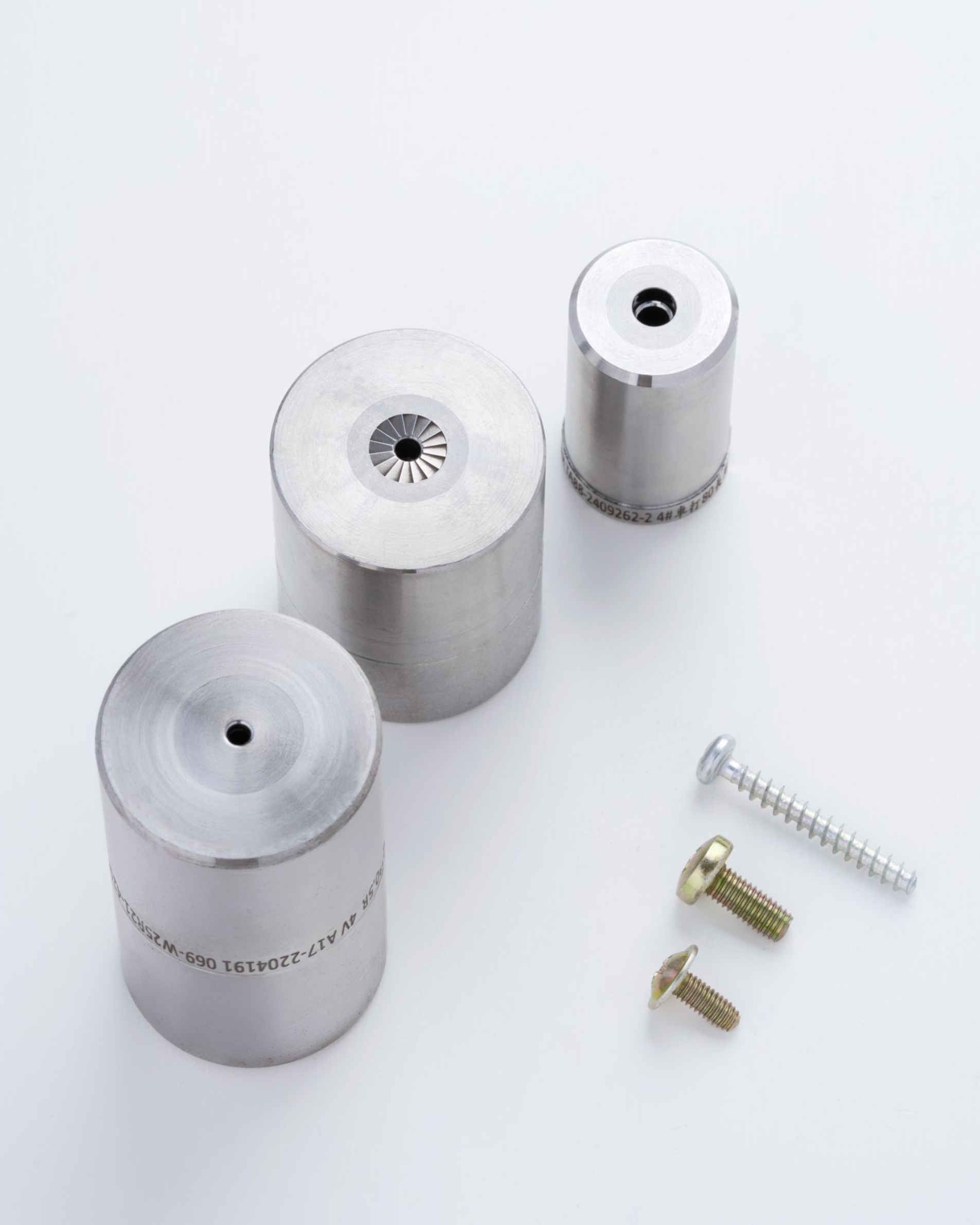 Three metal dies and three screws on a white surface.