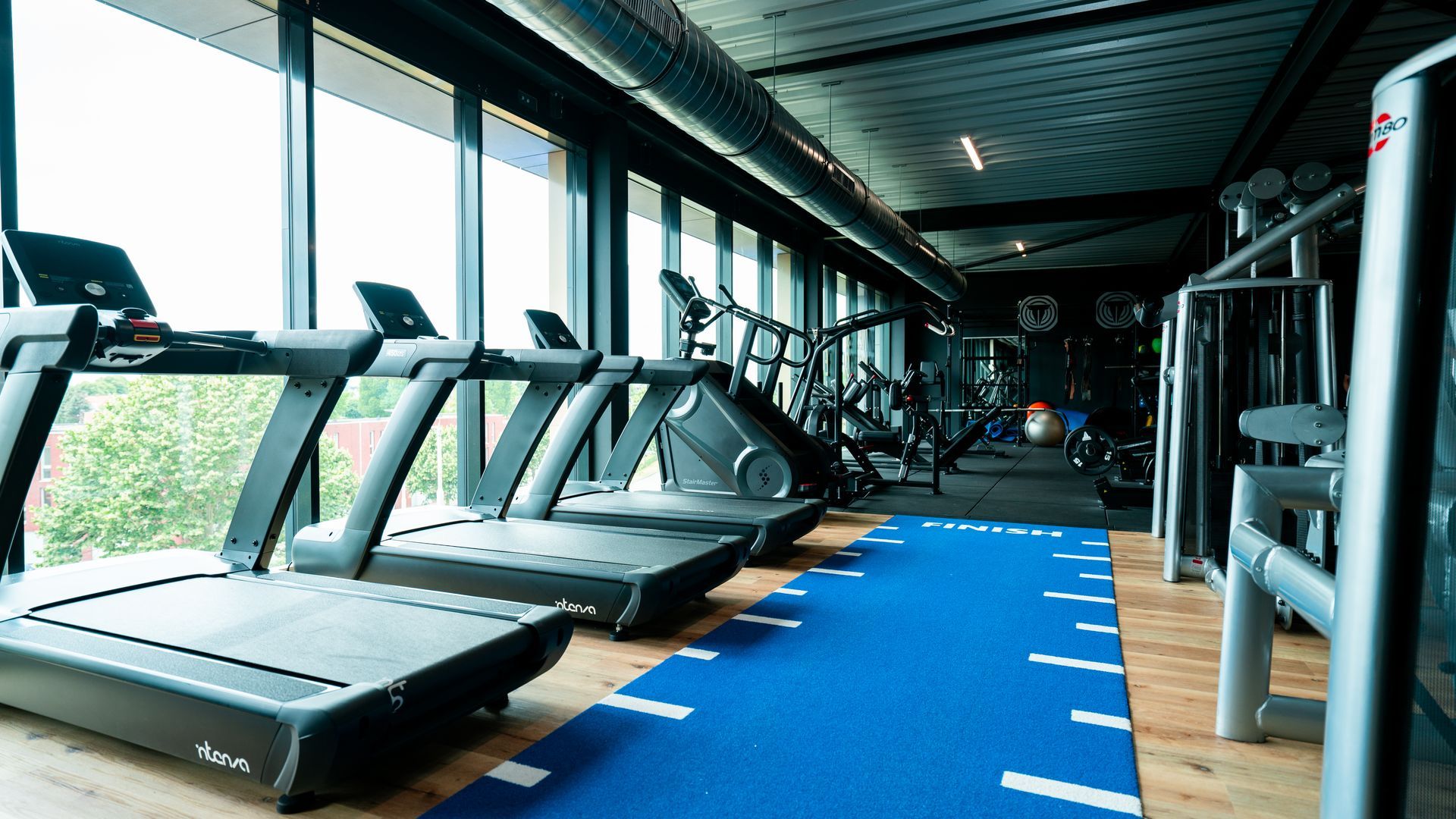 Een sportschool met loopbanden en een blauwe mat op de vloer.
