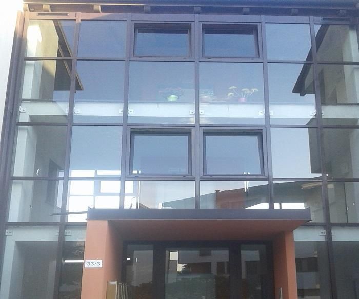 Ingresso di un moderno edificio con facciata in vetro, ampie finestre e una tenda da sole marrone