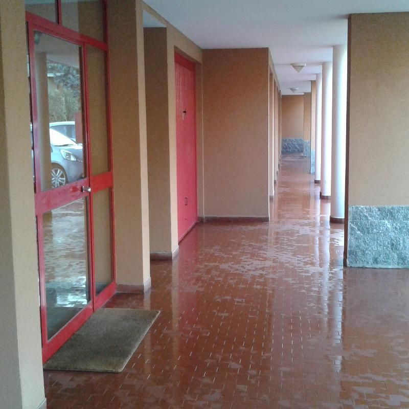 Lungo corridoio vuoto con porte rosse e finestre su un pavimento piastrellato bagnato