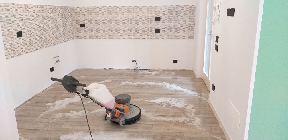 Cucina parzialmente piastrellata con una levigatrice per pavimenti e il pavimento coperto di polvere durante la ristrutturazione