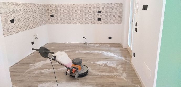 Cucina parzialmente piastrellata con una levigatrice per pavimenti e il pavimento coperto di polvere durante la ristrutturazione