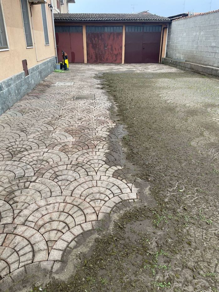 Cortile lastricato in modo irregolare accanto a una casa, con un cancello in metallo in fondo.