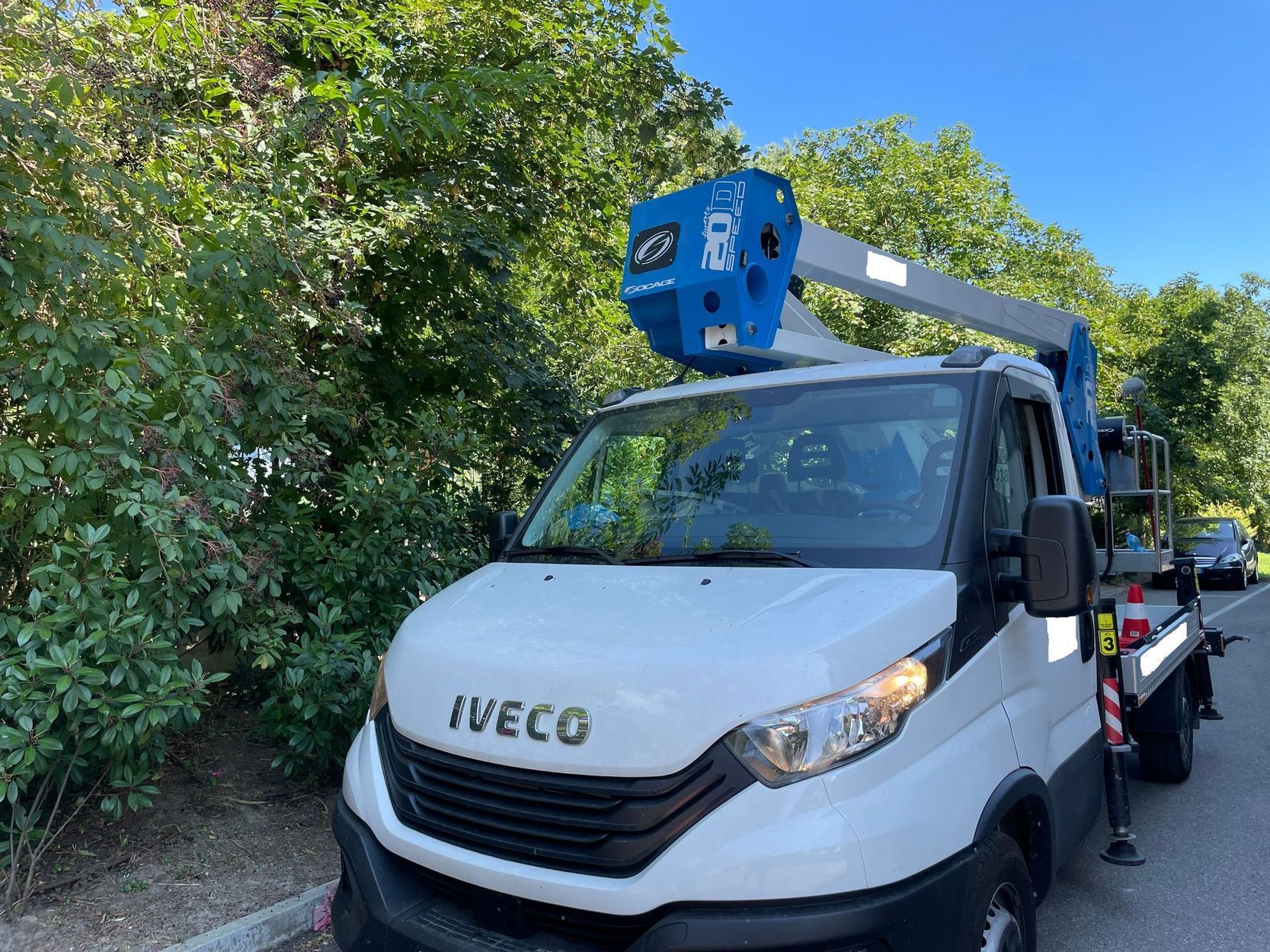 Furgone Iveco bianco con piattaforma aerea blu parcheggiato accanto agli alberi sotto un cielo sereno
