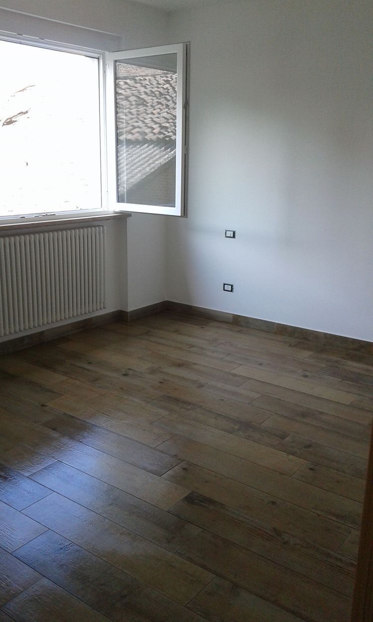 Stanza vuota con pavimento in legno, pareti bianche, finestra aperta e termosifone sotto la finestra.