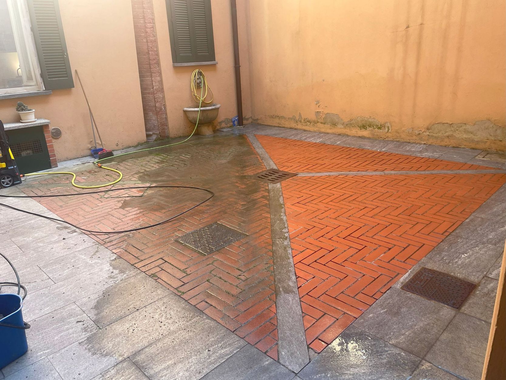 Cortile esterno con pavimentazione piastrellata bagnata, caratterizzato da un’ampia sezione arancione decorata a motivi e da pareti beige.