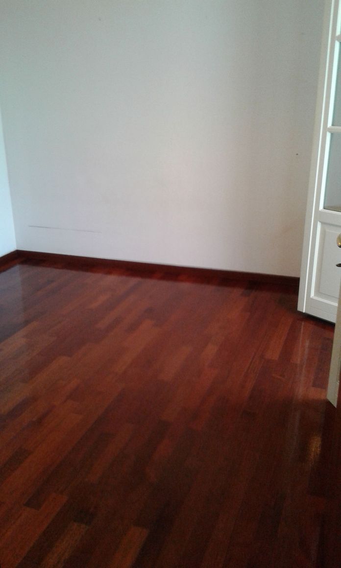 Stanza vuota con pavimento in parquet lucido, pareti bianche e stipite della porta sulla destra