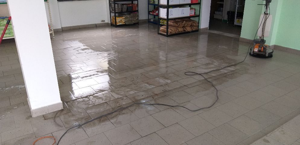 Pavimento interno piastrellato con un lungo cavo nero steso sopra, vicino a una colonna bianca e a degli oggetti impilati.