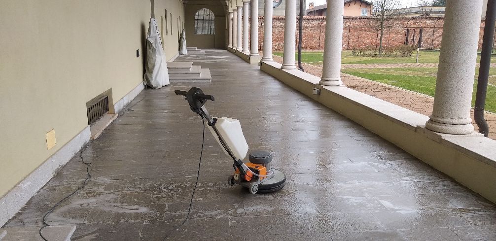 Soffiatore per foglie su un passaggio coperto bagnato, accanto a colonne bianche e a un edificio in mattoni