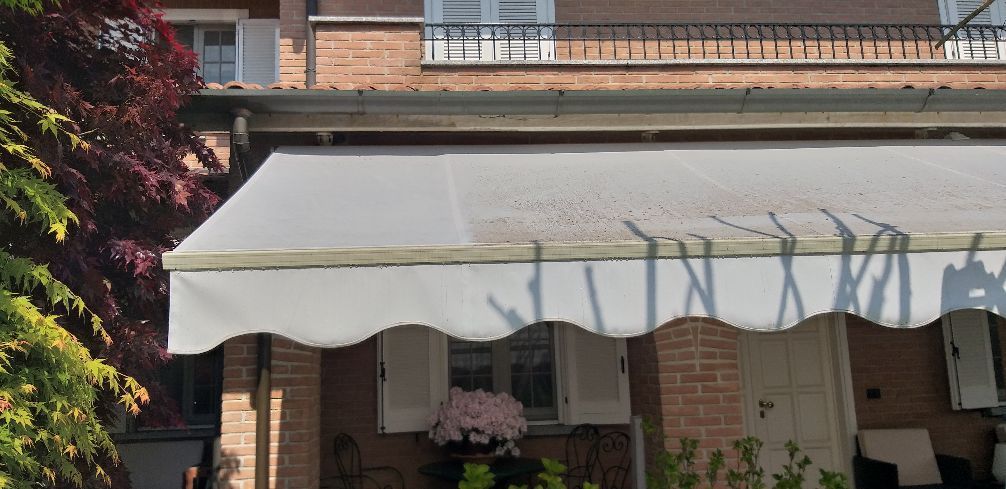 Casa in mattoni con un grande tendone bianco sopra un portico anteriore e fiori in vaso