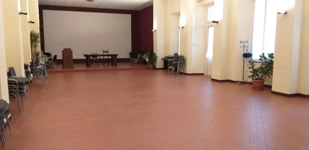 Lungo corridoio con pavimento in terracotta, pareti color crema, piante in vaso e un tavolo in fondo