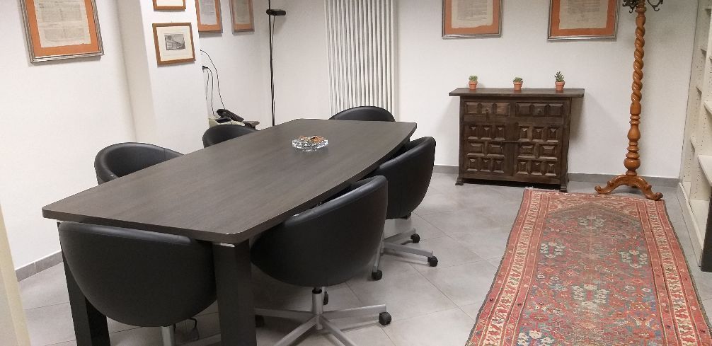 Sala conferenze con sedie nere attorno a un tavolo scuro, un mobile decorato e un tappeto a motivi geometrici