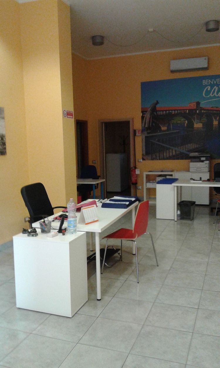 Piccolo ufficio con scrivanie bianche, sedie rosse e un poster da parete in una stanza dai toni caldi.