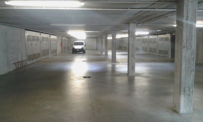 Parcheggio sotterraneo vuoto con colonne di cemento e un furgone bianco parcheggiato in lontananza