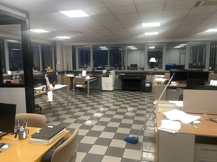 Ufficio disordinato con scrivanie, documenti e sedie sotto le luci fluorescenti