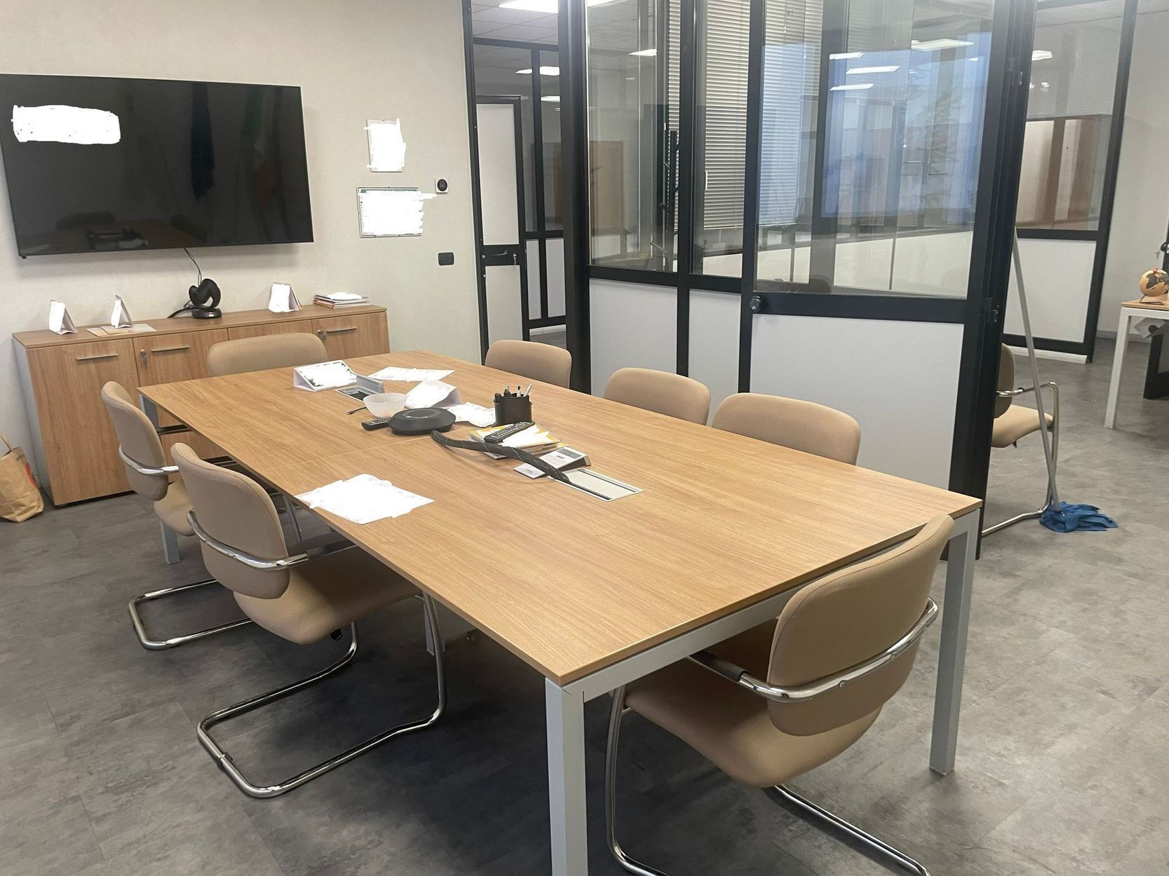 Sala riunioni moderna con tavolo in legno, sedie, TV a parete e pareti divisorie in vetro