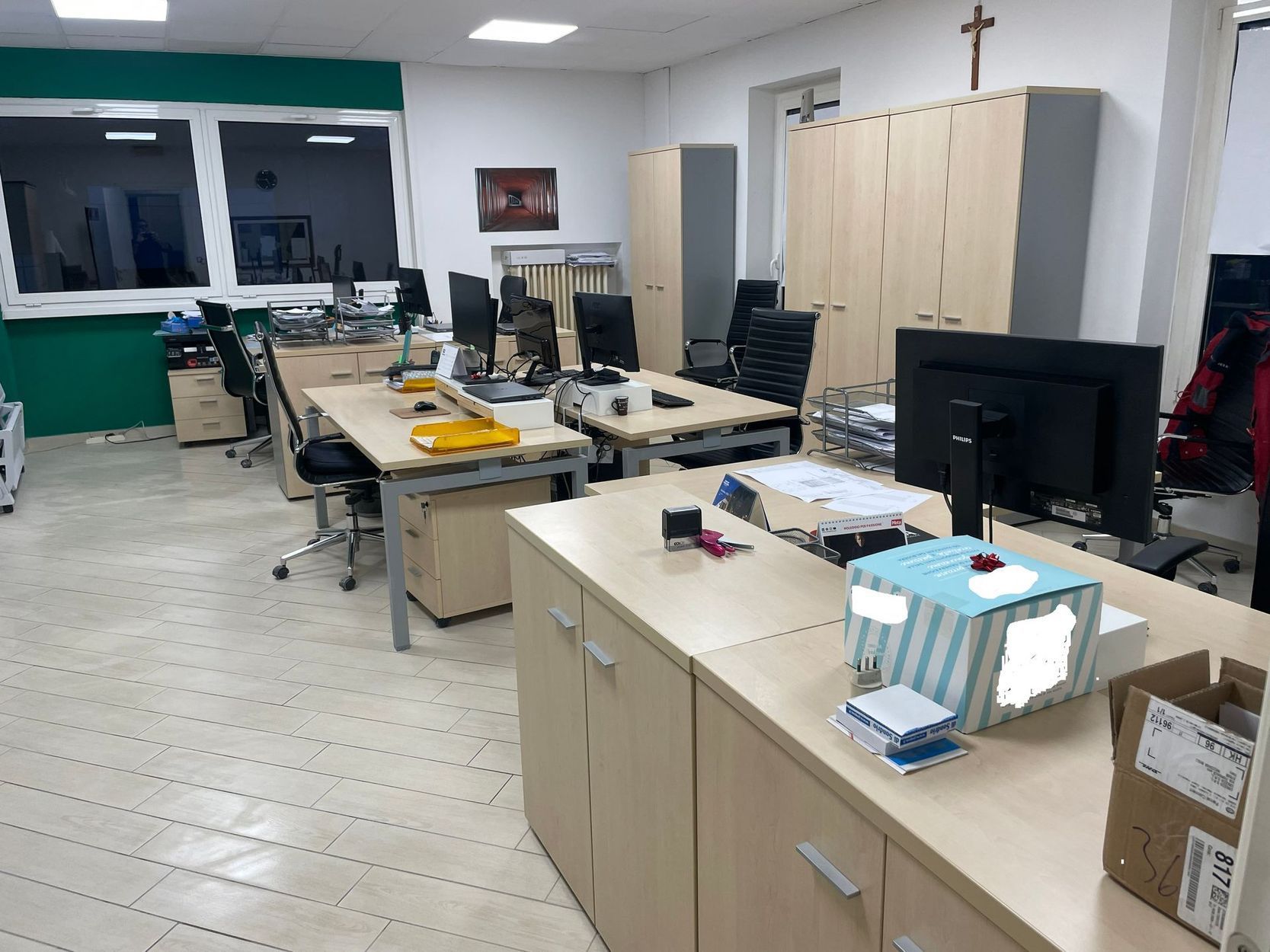 Spazio ufficio con scrivanie, monitor, armadietti e grandi finestre sul fondo
