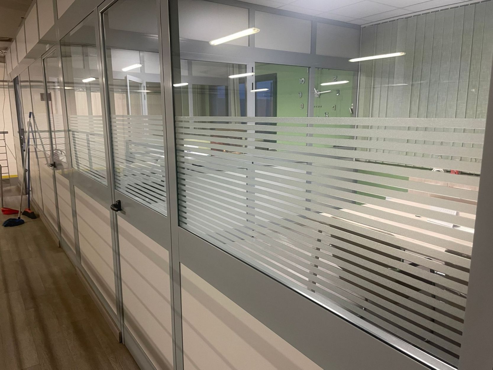 Corridoio di un ufficio con pareti divisorie in vetro satinato e pellicola decorativa a righe sulle finestre.
