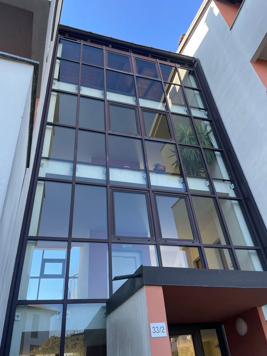 Ingresso di un edificio alto con facciata in vetro, sotto un cielo azzurro, con una tenda rossa sopra la porta.