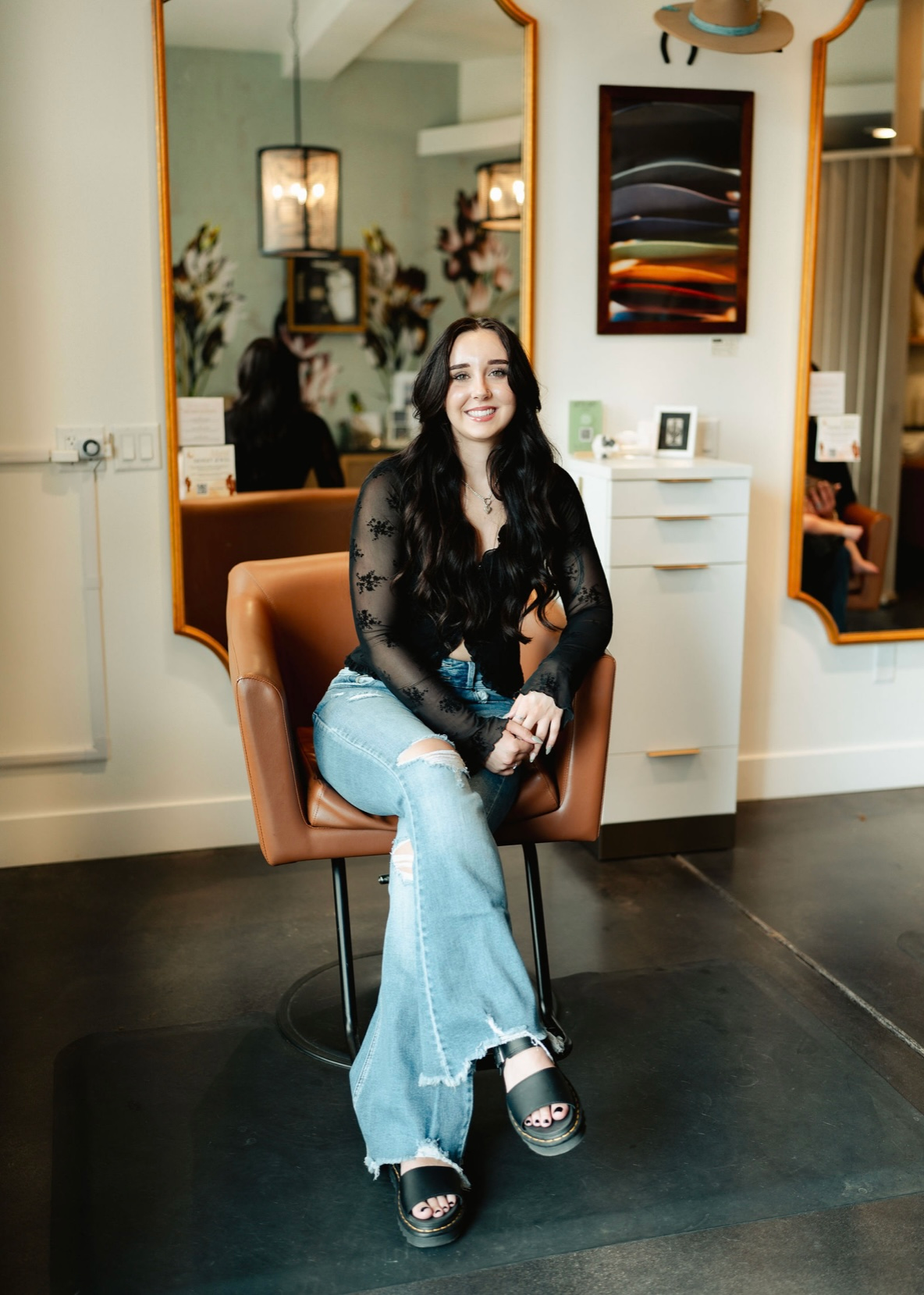 Smiling person seated in a tan chair in a modern room with mirrors and wall art