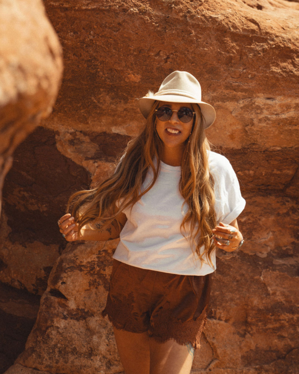 a woman wearing a hat and sunglasses stands in front of a wall