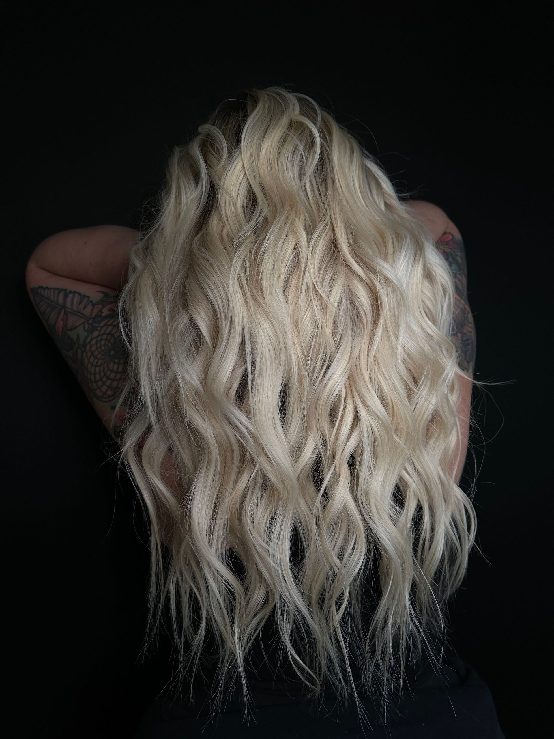 Person seen from behind with long wavy blonde hair against a dark background