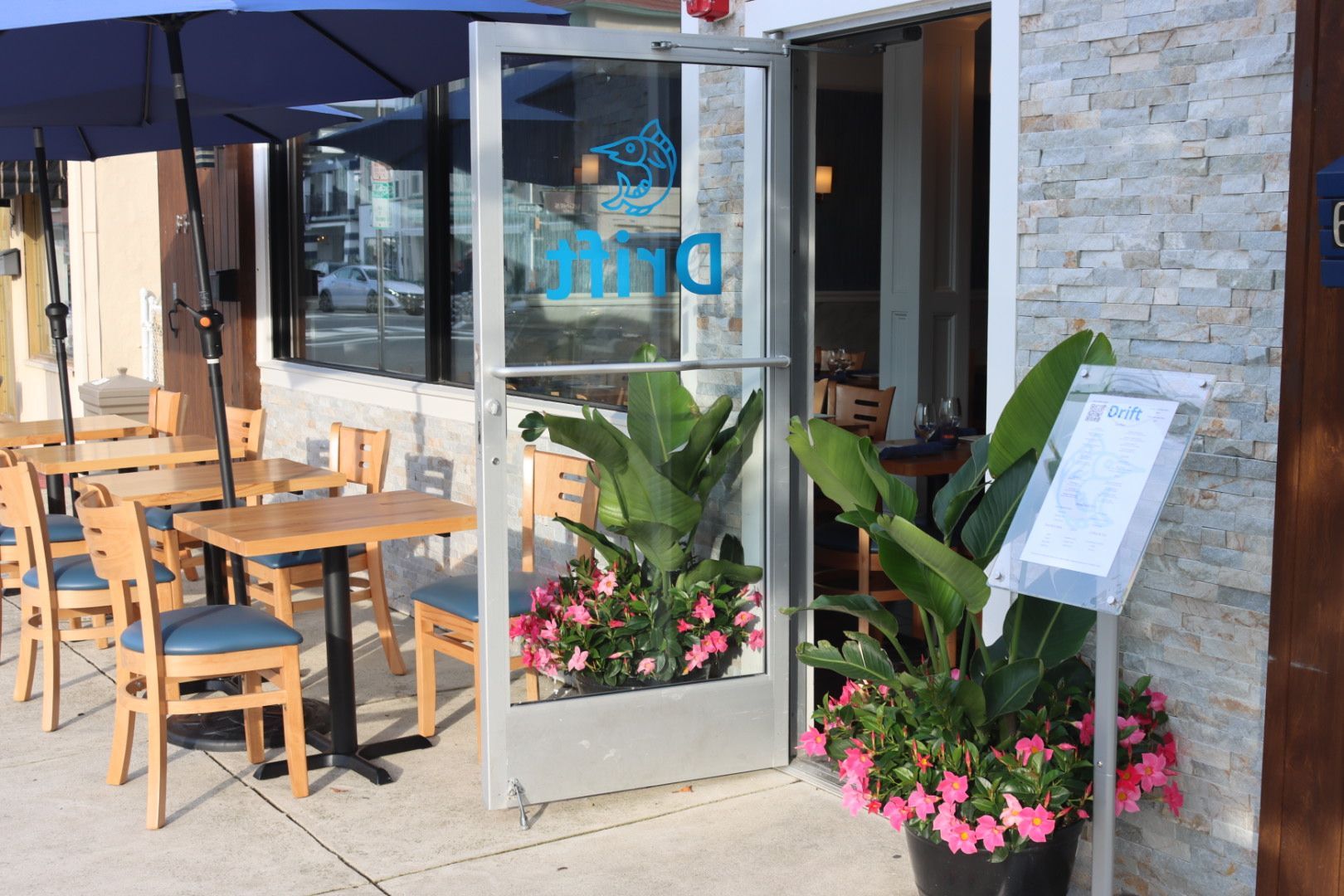 Front entrance to Drift Restaurant with tables, chairs, and umbrellas outside