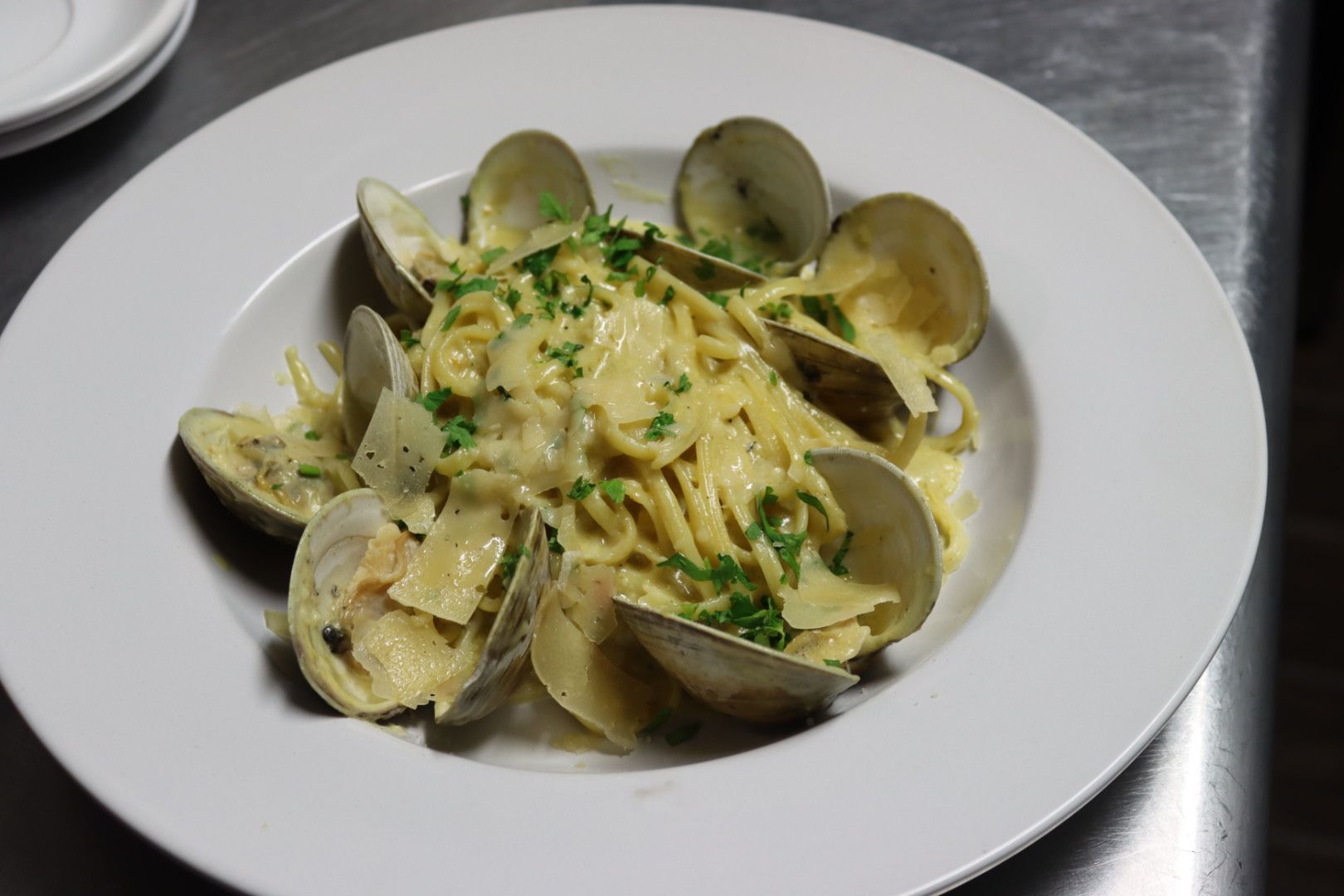 A white plate topped with clams and linguini with shaved parmesan cheese