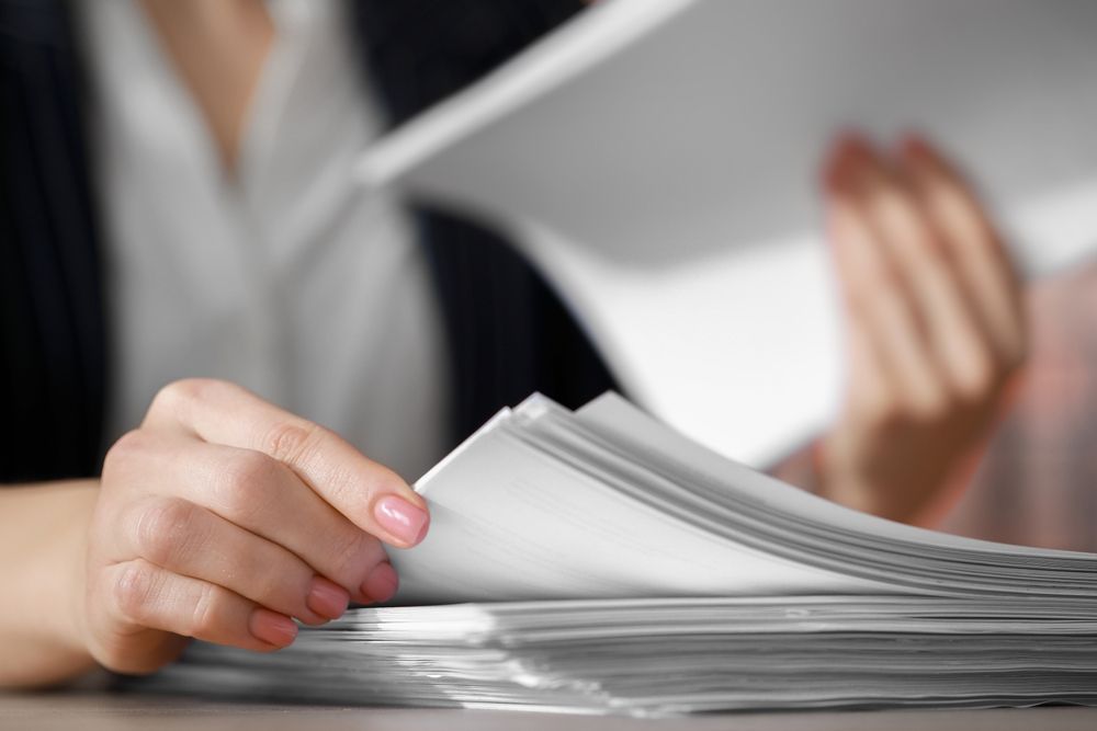 Woman's hands flipping through a stack of white papers, possibly documents, on a table — Immigration Agents in Cairns North, QLD