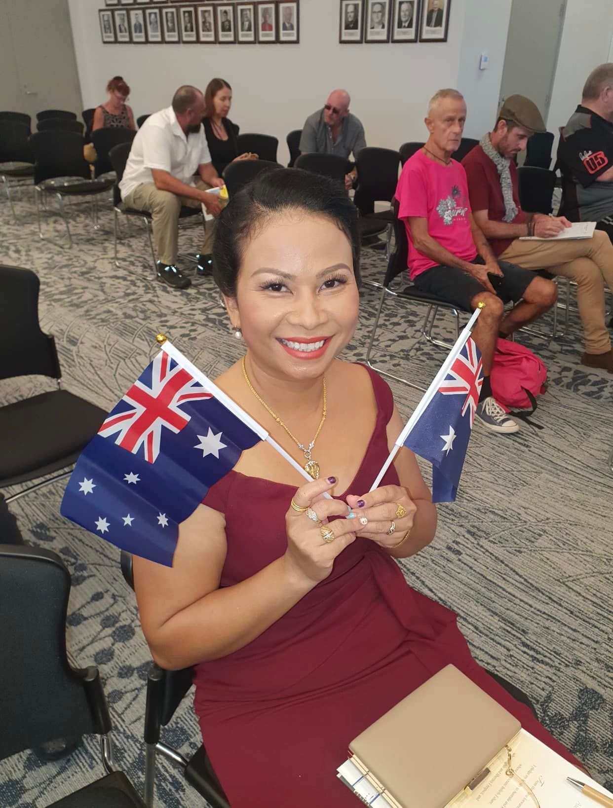 Woman in Burgundy Dress Smiles, Holding Two Australian Flags — Immigration Agents in Cairns North, QLD