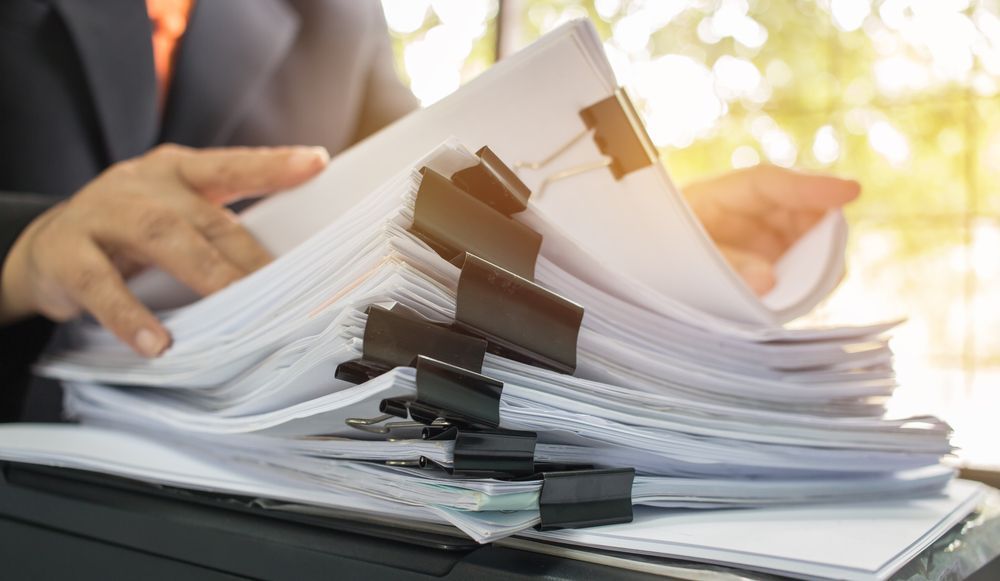 Person in suit, hands on a large stack of papers held together with clips, near a window — Immigration Agents in Cairns North, QLD