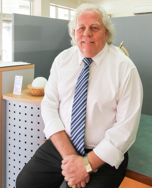 A Man With White Hair and a Blue Striped Tie Sits, Smiling in an Office — Immigration Agents in Cairns North, QLD