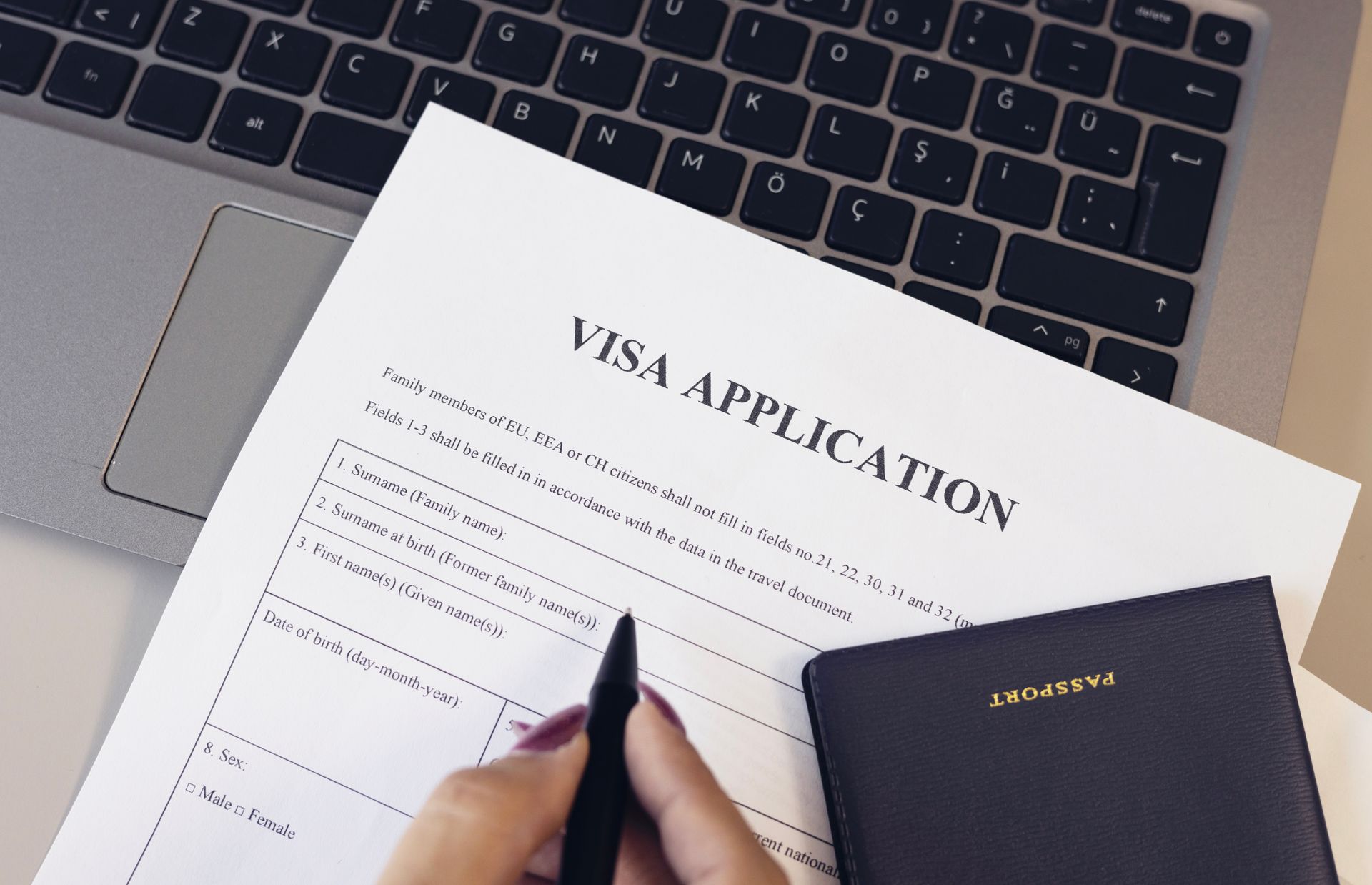 Hand Filling Out Visa Application Form With Laptop and Notebook on Desk — Immigration Agents in Cairns North, QLD